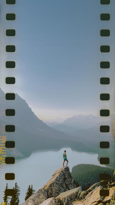 A man stands on a rocky peak overlooking a lake and mountains.