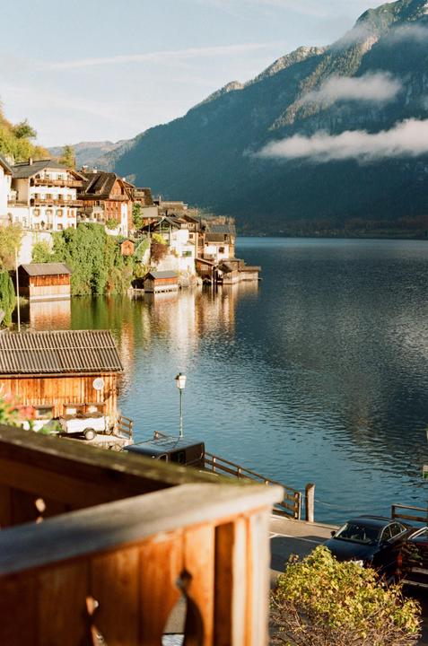A village with houses built into a mountainside overlooks a lake with reflections of the buildings and mountains.