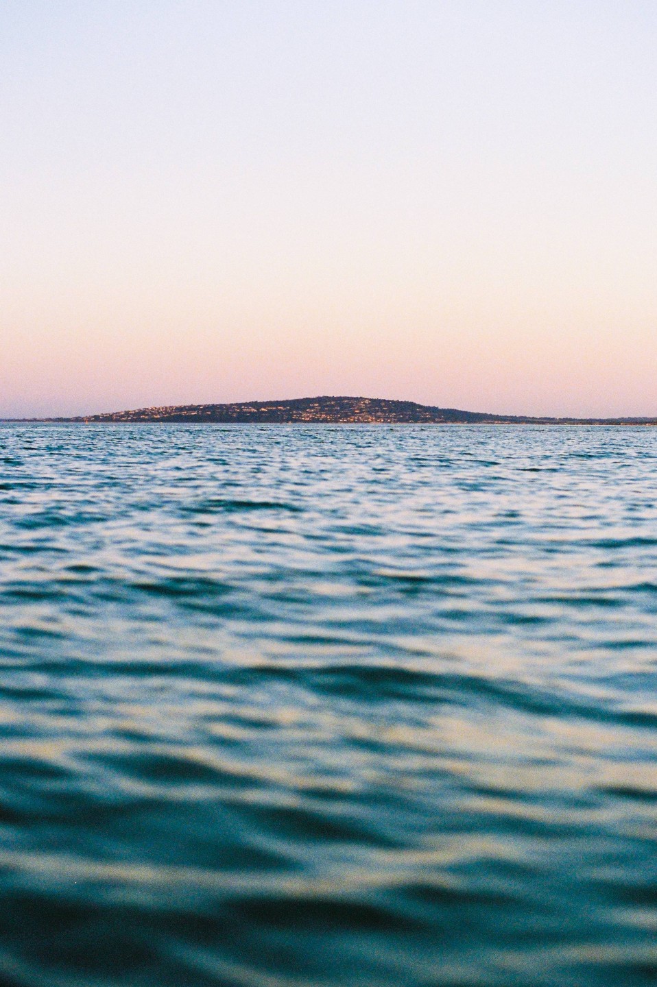 A body of water with small waves is in the foreground, and a distant landmass with lights is visible under a pale sky.