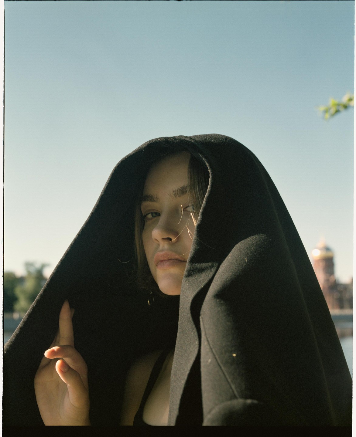 A woman with a black hood over her head looks at the viewer, with a golden dome building in the background.