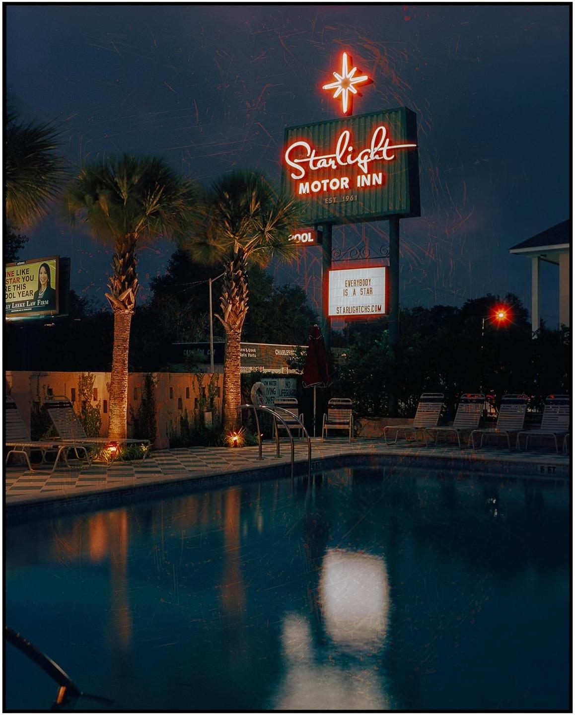 A neon sign for the Starlight Motor Inn stands beside a swimming pool and palm trees at night.