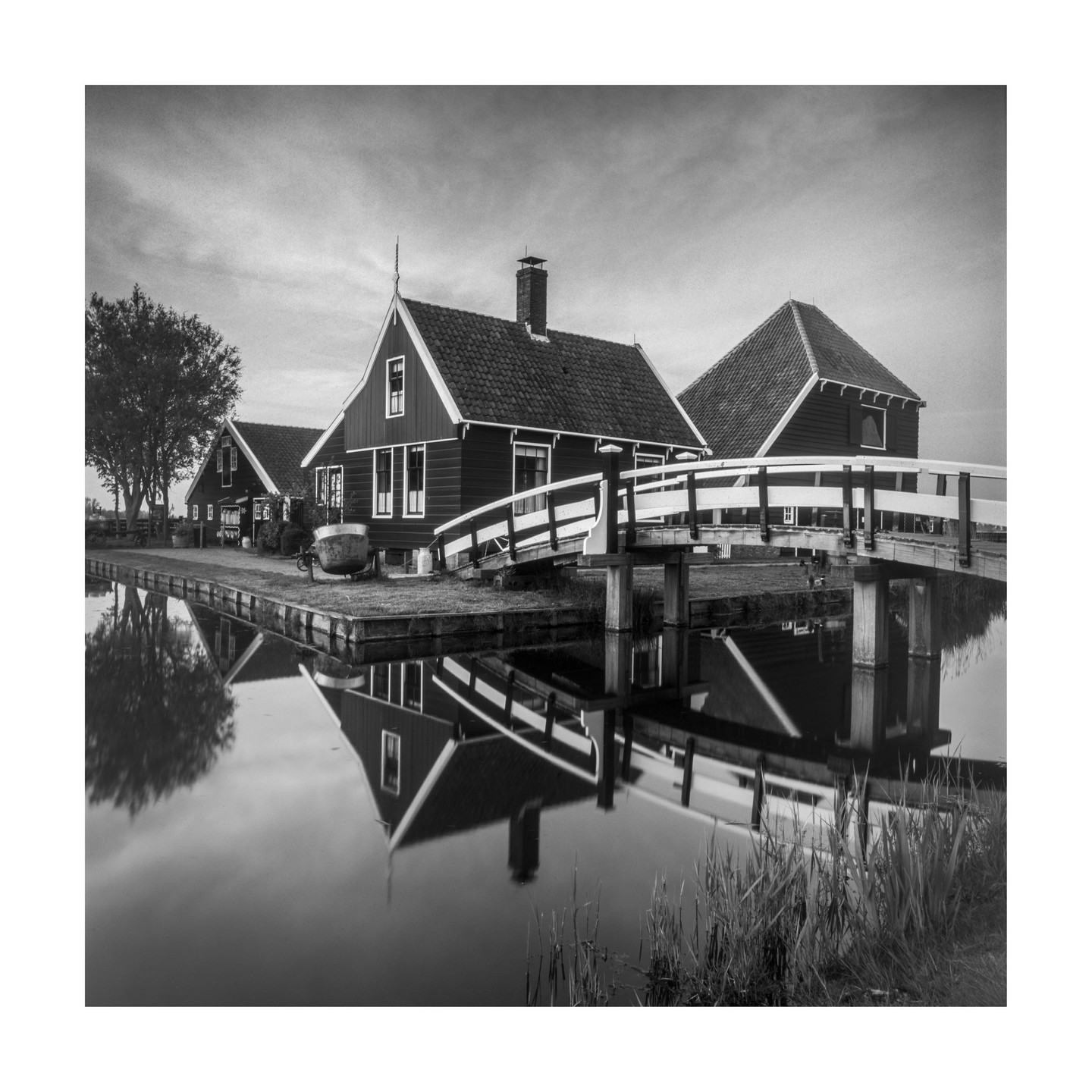 A black and white landscape shows houses and a bridge reflected in a canal.