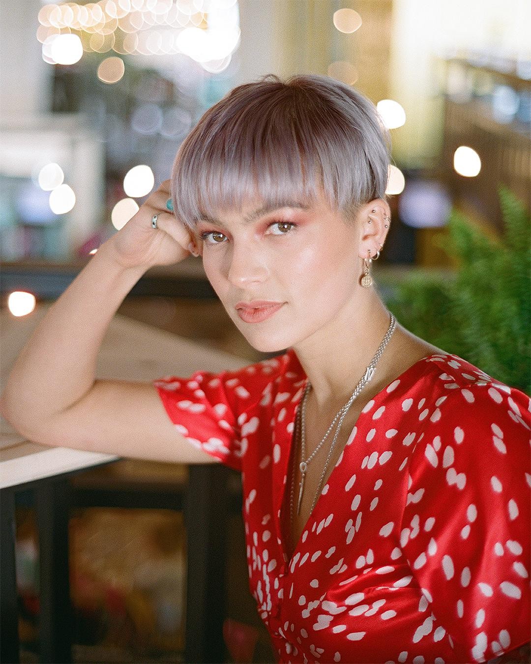 A woman with short hair and a red dress looks at the viewer.