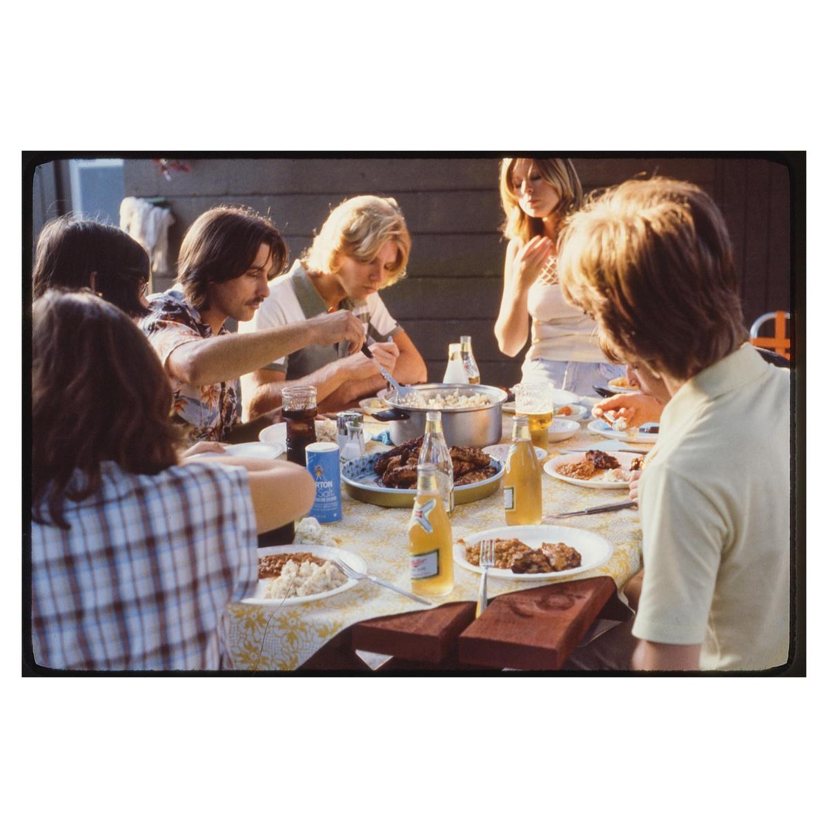 A group of people are gathered around a table laden with food and drinks, enjoying a meal together.
