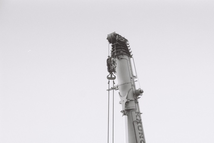 A crane boom with a hook and chains extends into a bright sky.
