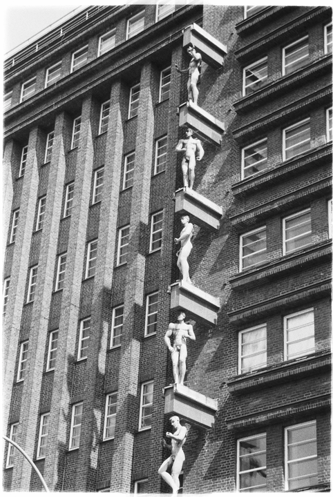 A tall brick building features a series of male statues on ledges along its facade.