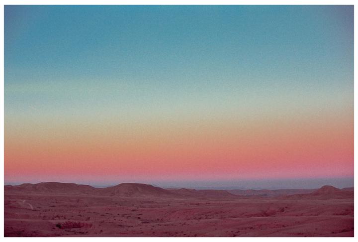 A desert landscape with rolling hills is visible under a sky with a colorful gradient.