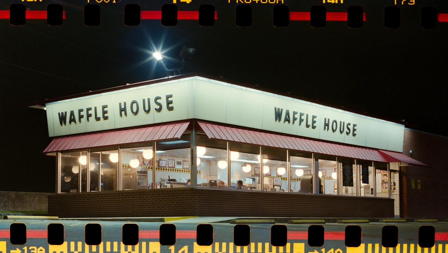 A Waffle House restaurant is brightly lit at night, with its sign prominently displayed and interior lights glowing through the windows.