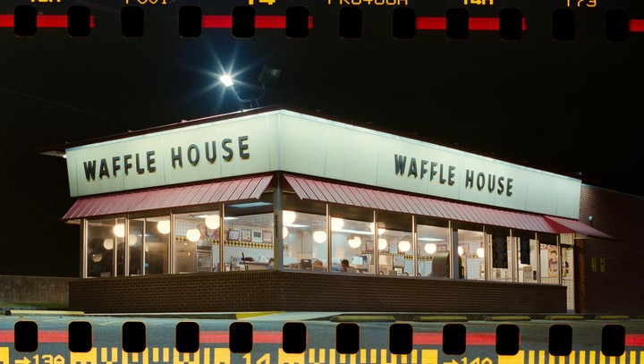 A Waffle House restaurant is brightly lit at night, with its sign prominently displayed and interior lights glowing through the windows.