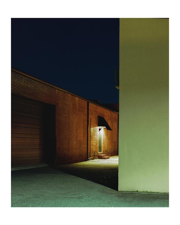 A brick building with a garage door and an illuminated doorway is visible at night.