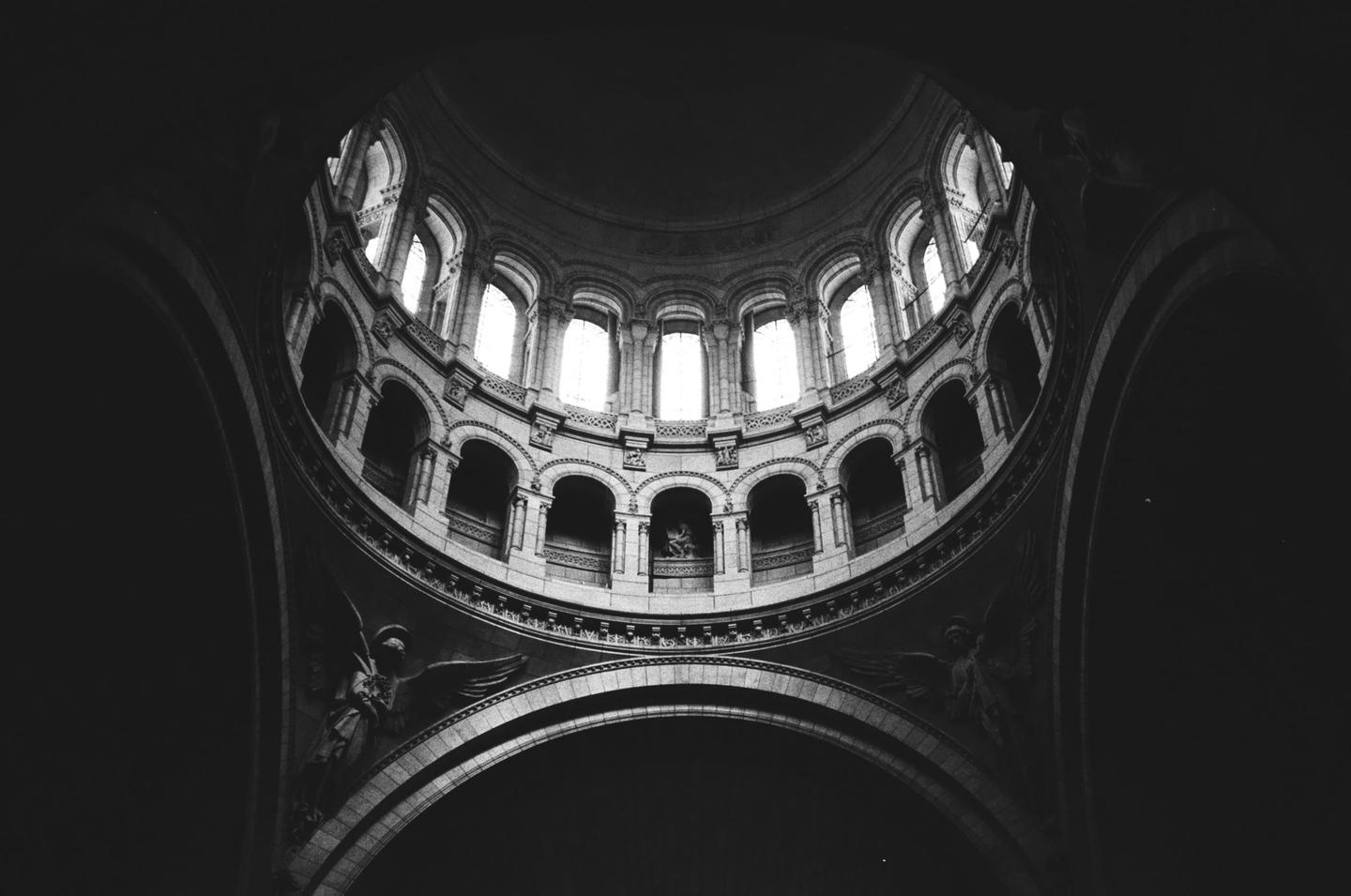 The interior of a large domed building with arched windows and sculptures is shown from below.