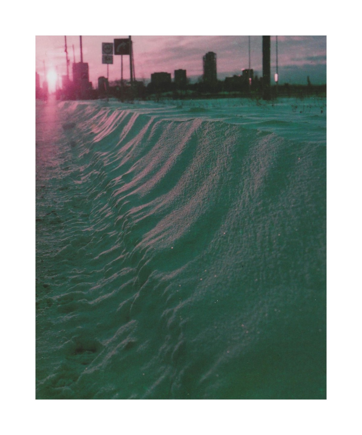 A snowdrift with a city skyline in the background is illuminated by a purple sky.