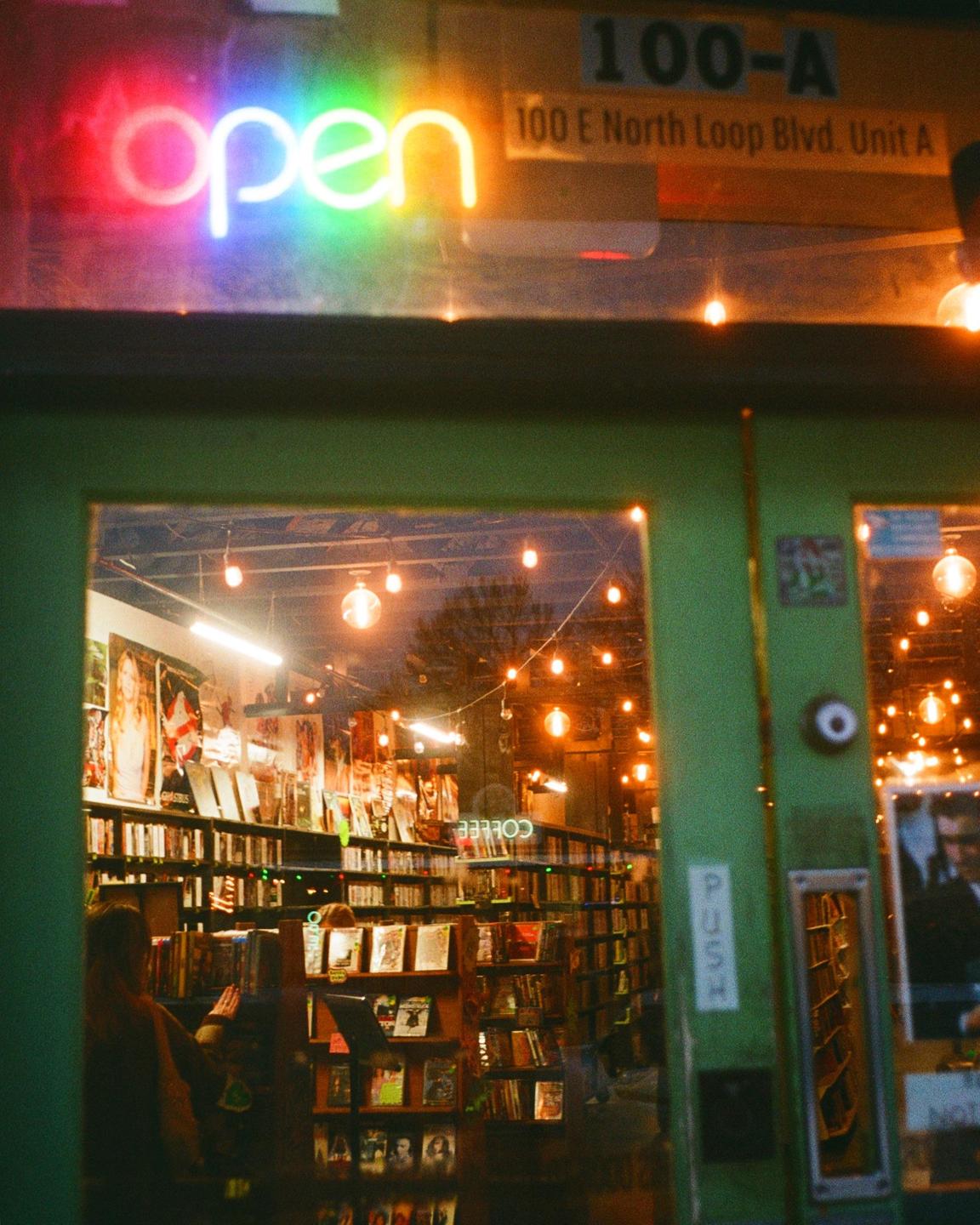 A neon "open" sign is visible above the entrance to a video store at night.