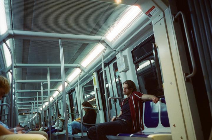 A man sits on a subway train at night, looking to his left.
