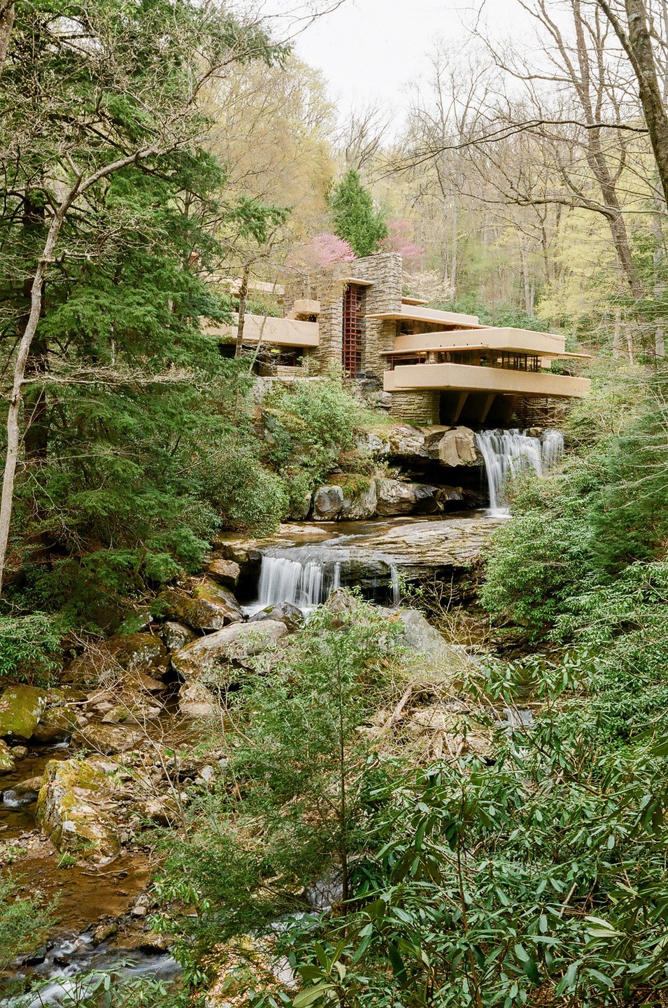 A house with multiple cantilevered levels is built over a waterfall in a forest.