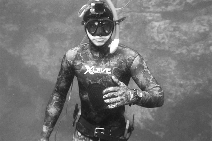 A man in a wetsuit, mask, and snorkel is underwater.