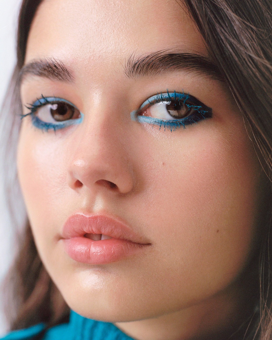 A woman with blue eyeliner and mascara looks directly at the viewer.