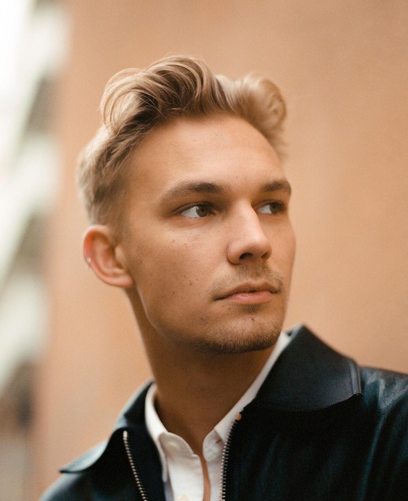 A man with blond hair and a light beard looks to the right of the frame.