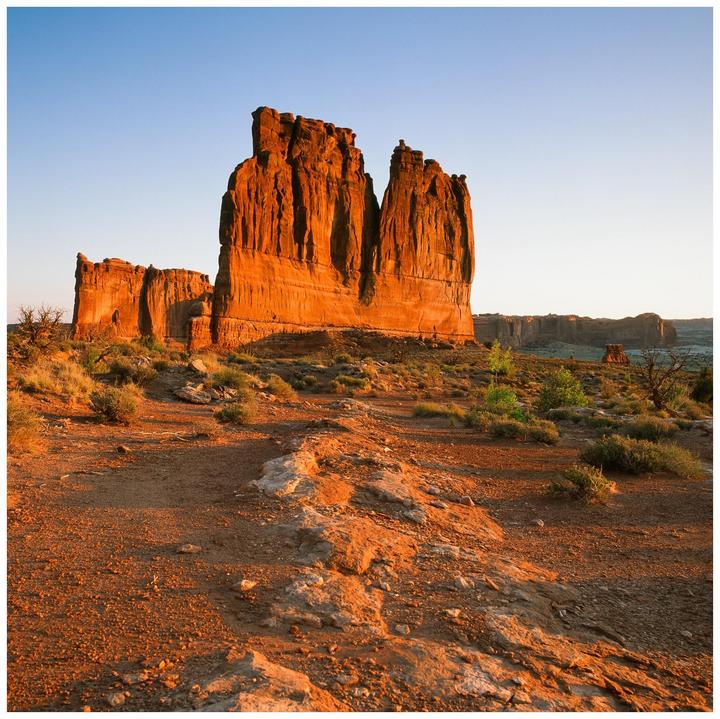 A large rock formation stands tall in a desert landscape under a clear sky.