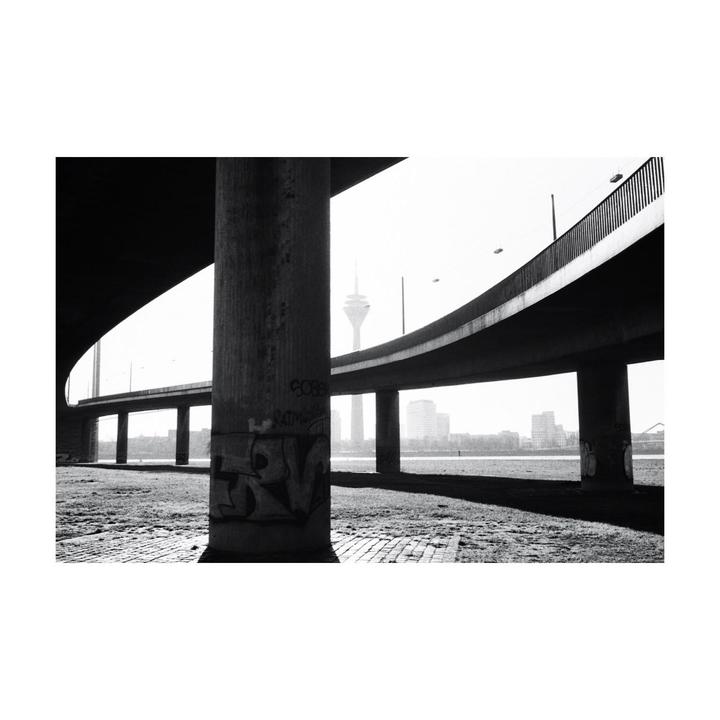 A television tower is visible in the distance through the arches of a concrete bridge.