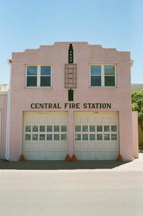 A pink building with "CENTRAL FIRE STATION" written on it has two garage doors and two windows.