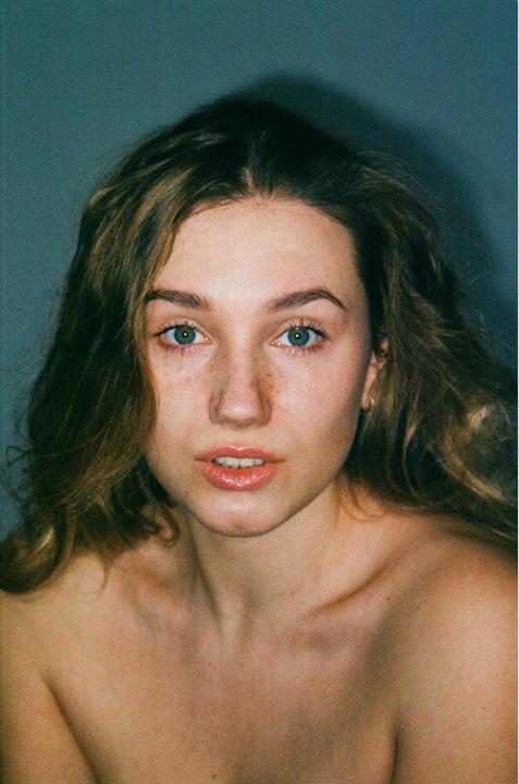 A woman with long hair and freckles looks directly at the viewer.