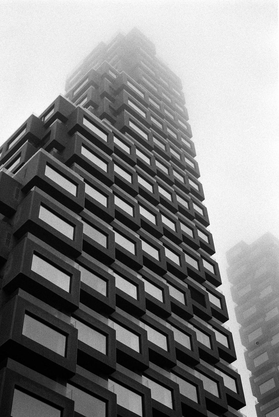 A tall building with a facade of rectangular windows is partially obscured by fog.