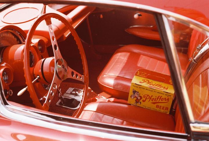 A red vintage car interior is visible through the window, with a box of Pfeiffer's beer on the passenger seat.