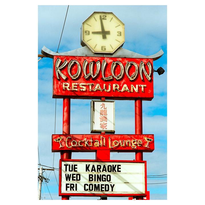 A red and white sign for Kowloon Restaurant and Cocktail Lounge stands against a blue sky.
