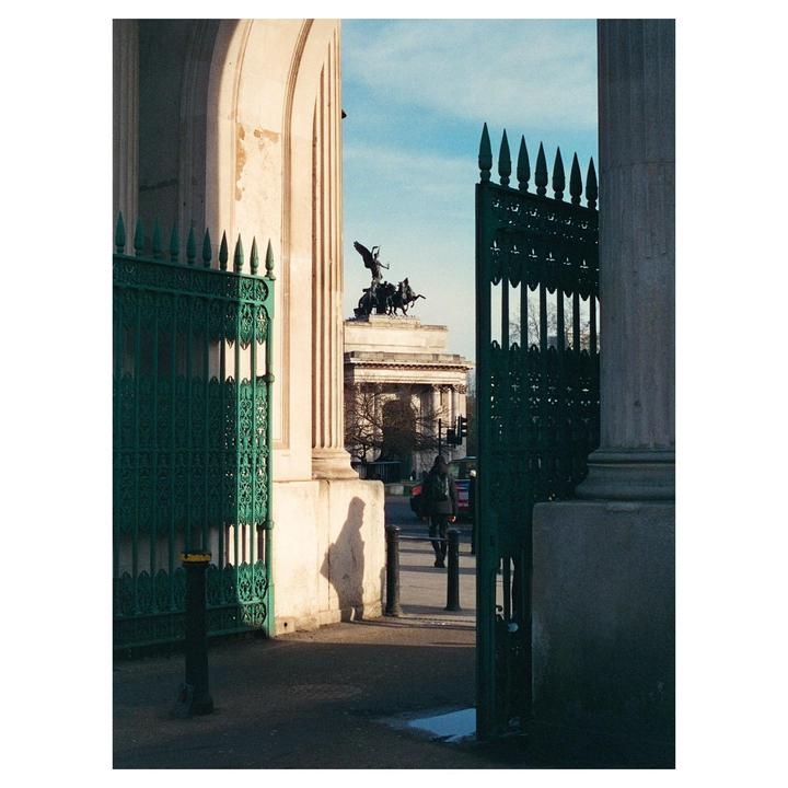 A person walks past a large green gate with a monument in the background.