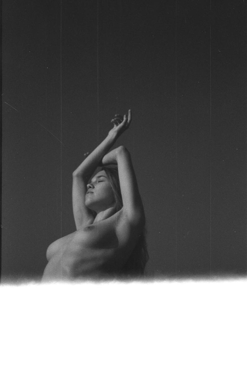A topless woman with her eyes closed and arms raised is visible in a black and white portrait.