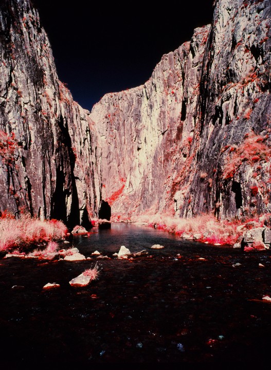 A narrow river flows between two tall, rocky cliffs under a dark sky.