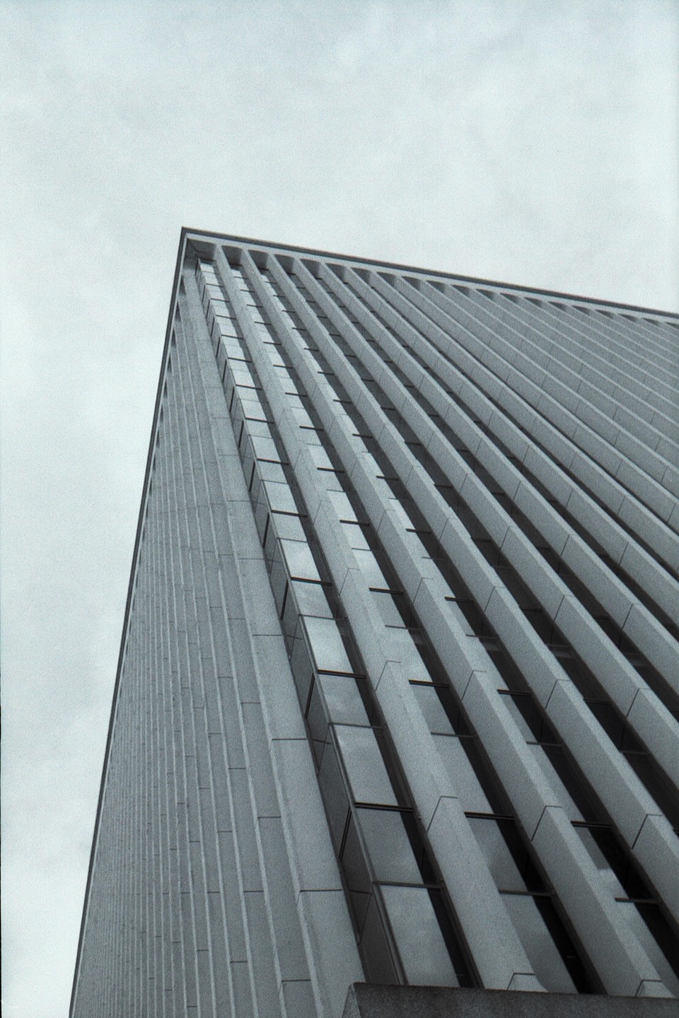 A tall building with many windows is viewed from a low angle against a light sky.