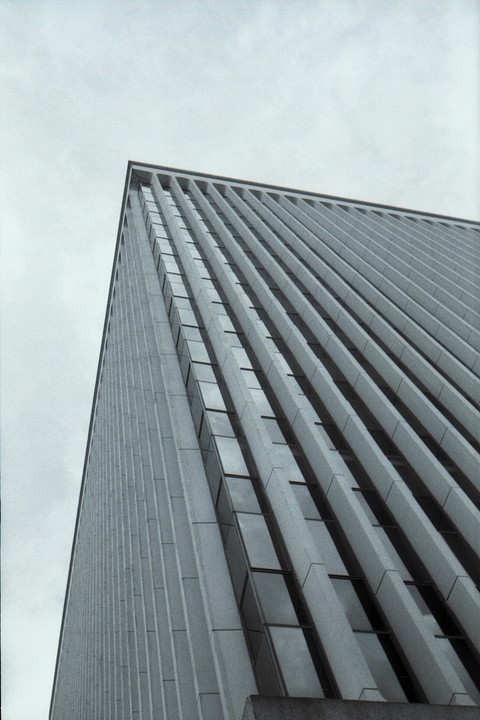 A tall building with many windows is viewed from a low angle against a light sky.
