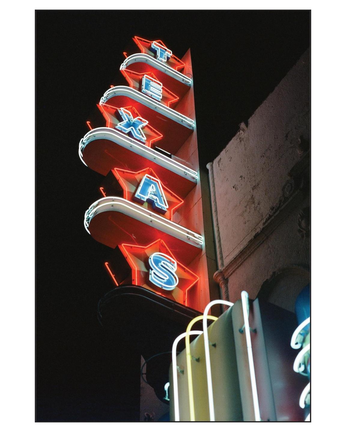 A neon sign spelling out "TEXAS" in red and blue letters is affixed to the side of a building at night.