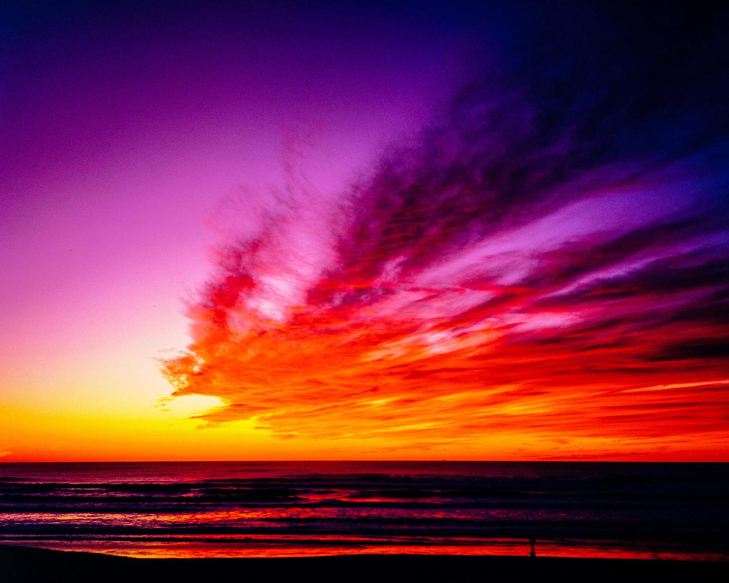 A vibrant sunset over the ocean shows a sky filled with red, orange, and purple clouds.