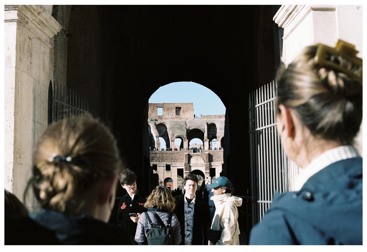 A group of people stand in a dark archway looking out at the Colosseum.