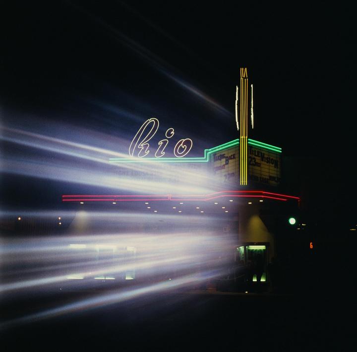 A building with neon signs is illuminated at night with light streaks across the frame.