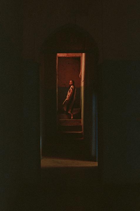 A woman stands on a staircase in a dimly lit room, looking towards the viewer.