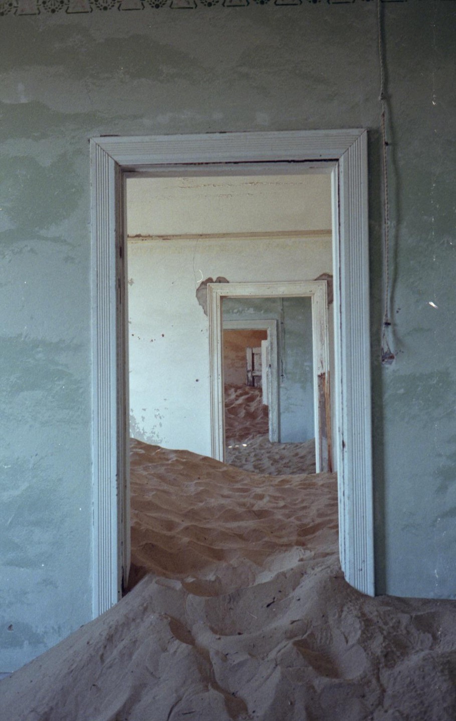 Sand fills a room and spills through a doorway into another room with more sand and doorways.