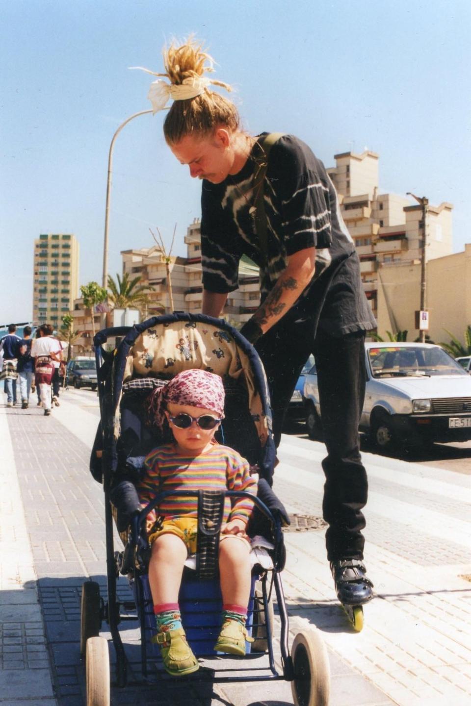 A man on rollerblades pushes a child in a stroller on a sunny street in Gibraltar.