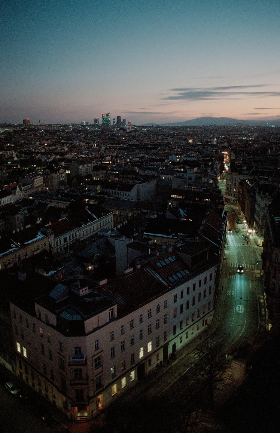 An aerial view shows a city at dusk with illuminated streets and buildings.