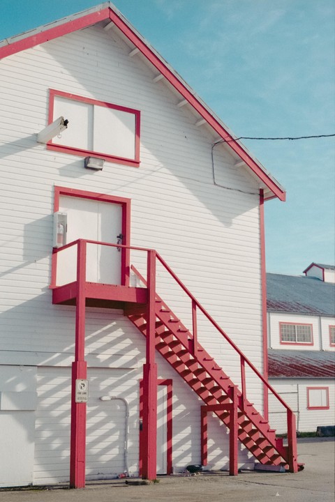 A white building with red trim and a red outdoor staircase is shown under a clear blue sky.