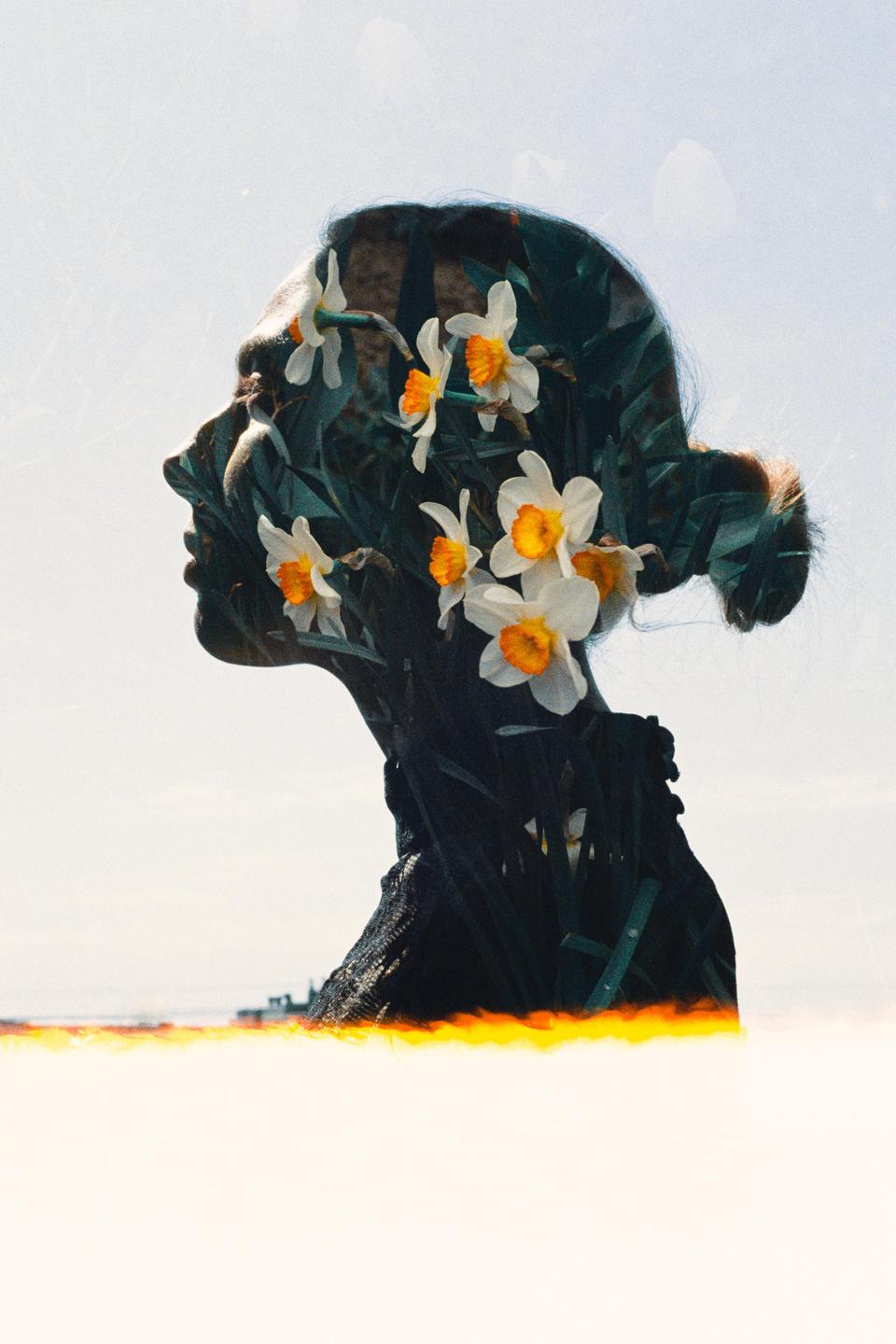 A woman's profile is double exposed with white and orange flowers and green foliage.