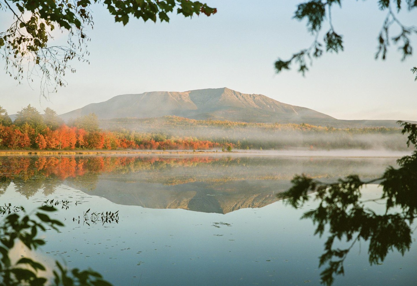 A mountain reflects in a misty lake surrounded by autumn foliage.