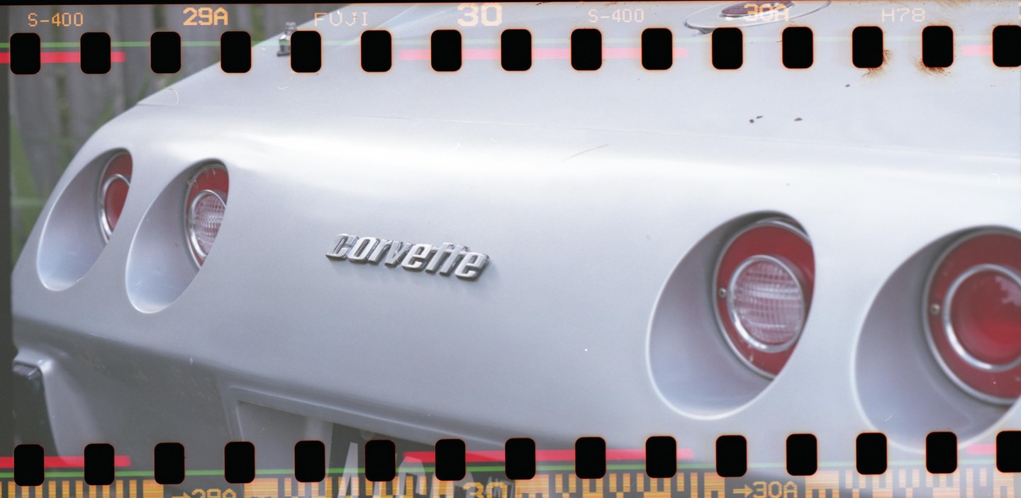 The rear of a silver Corvette is visible, showing its taillights and emblem.