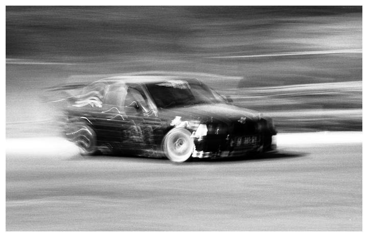 A black car is captured in motion blur on a track.