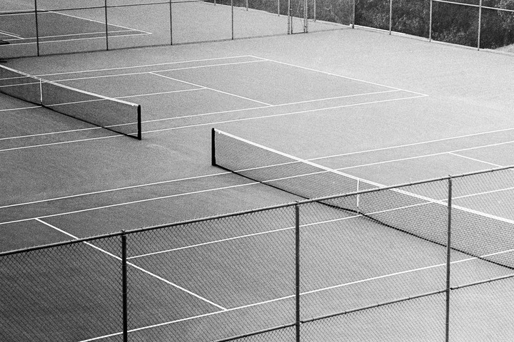An elevated view shows two tennis courts with nets and surrounding chain-link fences.