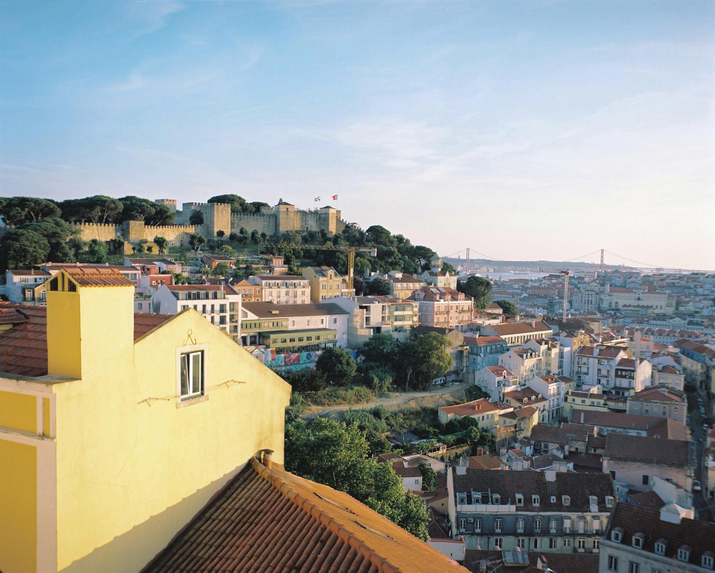 A panoramic view of a city with a castle on a hill and a suspension bridge in the distance.