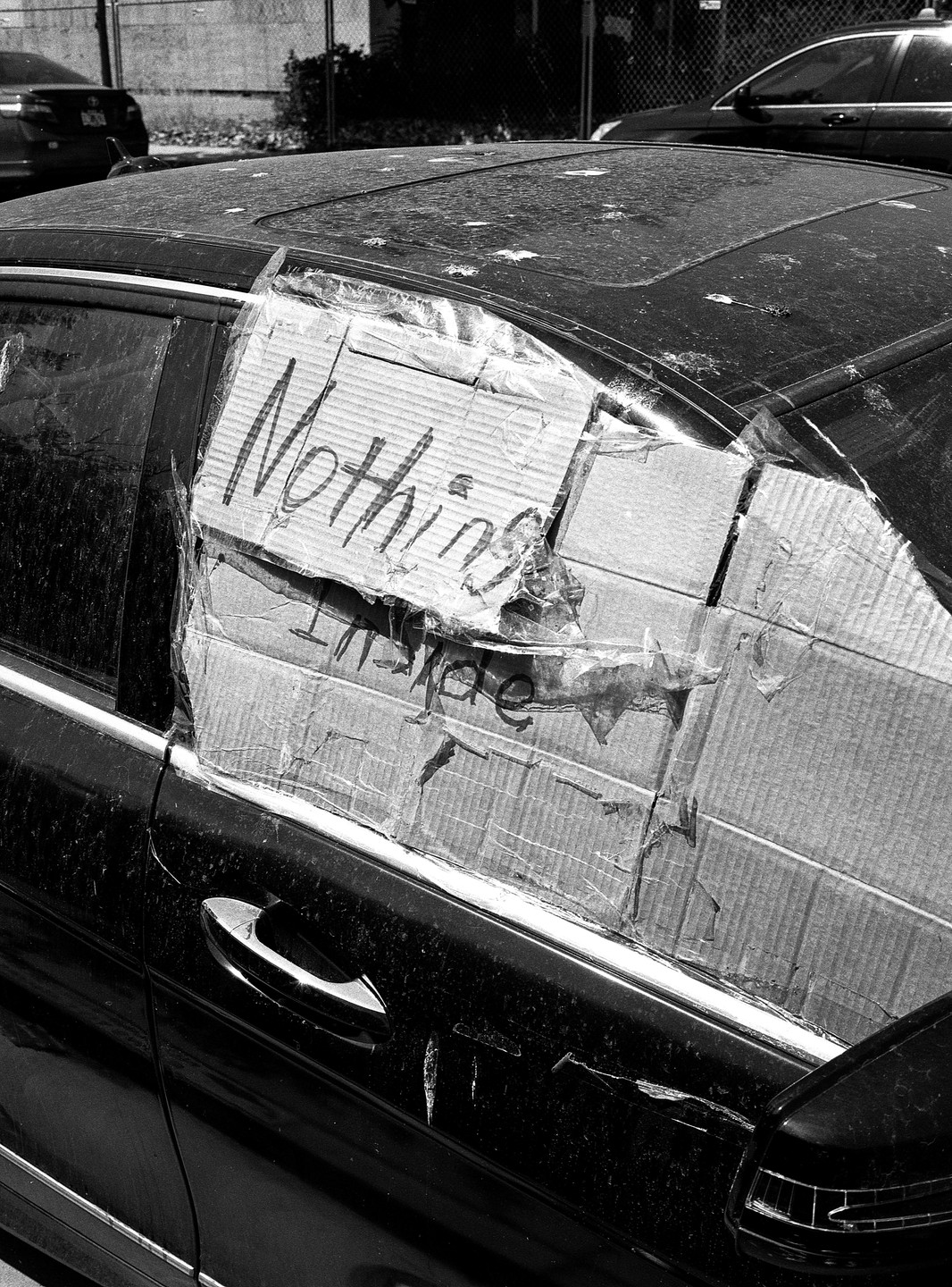 A car with a broken window is covered with cardboard and tape, with the word "Nothing" written on it.